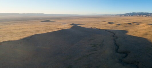 Aerial view of a dry riverbed cutting through the arid landscape of Carrizo Plain National Monument in California, USA. Mountains are visible in the distance.