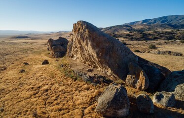 Scenic landscape of Carrizo Plain National Monument, California, USA. Large rock formations dot the golden, grassy hills under a clear blue sky.