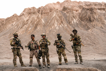 Special Forces Team Standing Together in Desert Mountain Terrain – Tactical Soldiers in Full Gear...