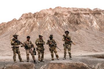 Special Forces Team Standing Together in Desert Mountain Terrain – Tactical Soldiers in Full Gear with Rifles, Communicating and Coordinating During a Military Operation or Training Mission