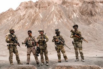 Special Forces Team Standing Together in Desert Mountain Terrain – Tactical Soldiers in Full Gear...