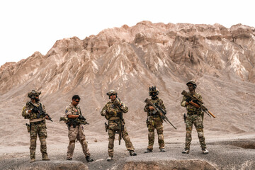 Special Forces Team Standing Together in Desert Mountain Terrain – Tactical Soldiers in Full Gear...
