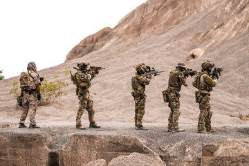 Special Forces Team Standing Together in Desert Mountain Terrain – Tactical Soldiers in Full Gear...