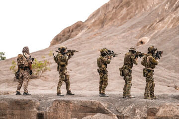 Special Forces Team Standing Together in Desert Mountain Terrain – Tactical Soldiers in Full Gear...