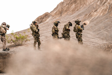 Special Forces Team Standing Together in Desert Mountain Terrain – Tactical Soldiers in Full Gear...