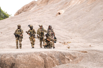 Fototapeta premium Special Forces Team Standing Together in Desert Mountain Terrain – Tactical Soldiers in Full Gear with Rifles, Communicating and Coordinating During a Military Operation or Training Mission