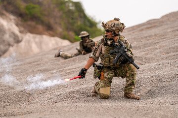 Fototapeta premium Special forces soldier uses a radio during a tactical operation while red flare smoke spreads across the rocky ground. Team communicates under high-alert battlefield conditions.