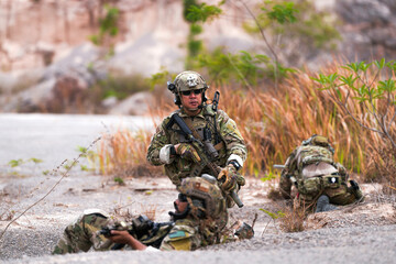 Fototapeta premium Special forces soldier uses a radio during a tactical operation while red flare smoke spreads across the rocky ground. Team communicates under high-alert battlefield conditions.