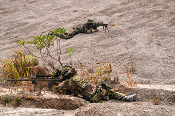 Two Sniper Soldiers in Camouflage Gear Aiming from Concealed Positions on Rocky Terrain –...