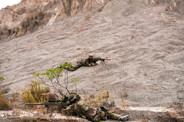 Two Sniper Soldiers in Camouflage Gear Aiming from Concealed Positions on Rocky Terrain –...