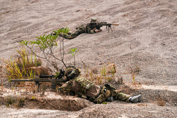 Two Sniper Soldiers in Camouflage Gear Aiming from Concealed Positions on Rocky Terrain –...