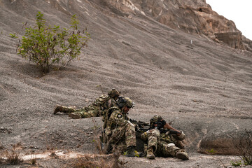 Two Sniper Soldiers in Camouflage Gear Aiming from Concealed Positions on Rocky Terrain –...
