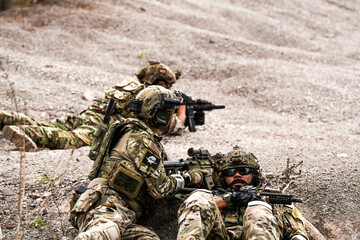 Two Sniper Soldiers in Camouflage Gear Aiming from Concealed Positions on Rocky Terrain –...