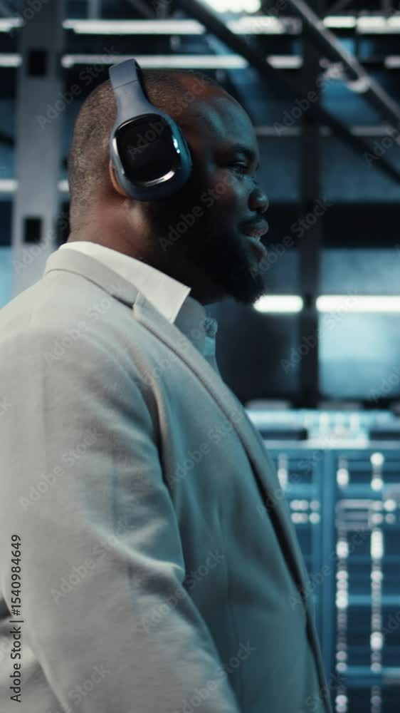 Poster vertical video happy worker wearing headphones walking in data center with hardware used to host web