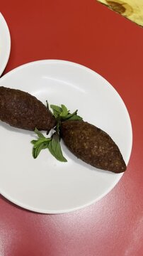 4k vertical video in a traveling motion of a delicious traditional Lebanese food, hummus and kibbe, served on white plates in a Lebanese restaurant.	
