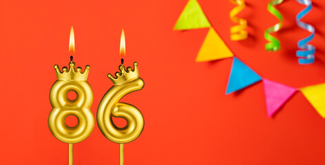 Number 86 birthday candle on an orange background with pennants