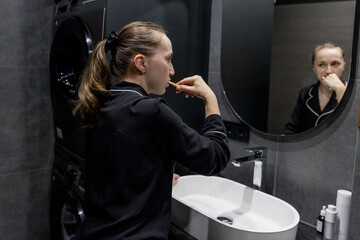 A woman in comfy pajamas brushes her teeth in a modern bathroom, enjoying her daily selfcare routine. Morning Routine