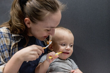 A woman with her baby brushes her teeth while holding a baby in hands in the bathroom