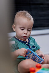 A small baby is happily sitting on the floor and playing with a toy phone