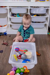 A small baby is happily playing with colorful toys in a white bin