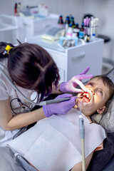 Children's dentistry. First examination at the dentist. A cute handsome boy with his mouth open is looking aside while the doctor is treating her teeth.