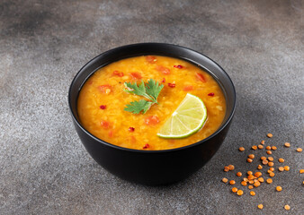 Red lentil soup with spices and fresh herbs on a gray background. Indian dal soup.