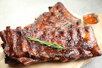 Tasty roasted pork ribs served with rosemary and sauce on light grey table, closeup