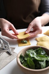 Woman making ravioli with cheese and spinach at white table, closeup