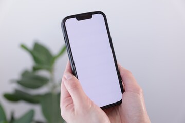 Woman holding smartphone with blank screen on blurred background, closeup. Mockup for design