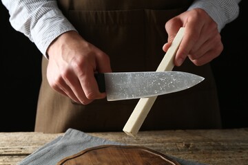 Man sharpening knife with sharpener on wooden table, closeup