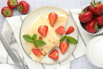 Tasty crepes with cream, strawberries and mint served on light gray textured table, flat lay