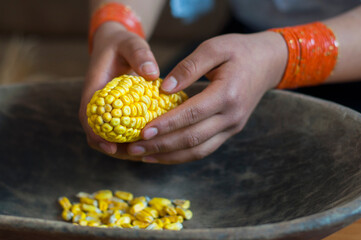 Woman shelling corn kernels into a wooden bowl