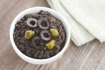 Homemade french black olive tapenade spread garnished with olive slices and capers, served in a...