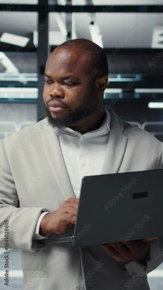 Poster vertical video technician walking in data center, using laptop to check hardware for system stabilit