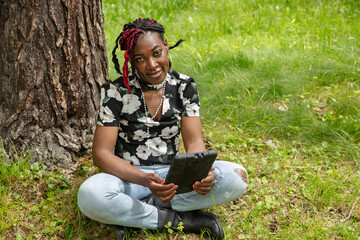 African American Student with Colorful Braids Using Digital Tablet in Park for Learning
