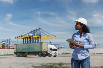 A female engineer in a safety helmet uses a digital tablet while monitoring container logistics at...