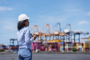 A female customer or logistics coordinator observes operations at a shipping port, holding a radio...