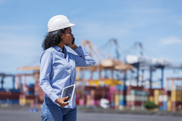 A female customer or logistics client at a shipping port talks on the phone while holding a tablet....