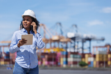 A female customer or logistics client at a shipping port talks on the phone while holding a tablet....
