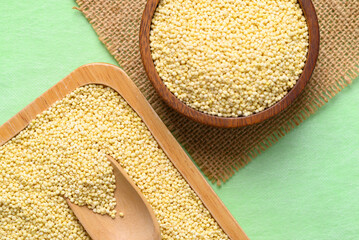 Yellow millet grain in wooden bowl and plate on green background, Food ingredient, Top view