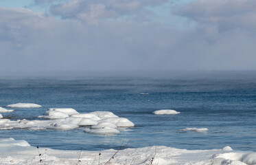 Snow and ice in blue lake with steam on horizon