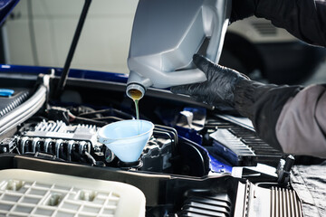 Worker pouring motor oil from canister into car engine, closeup
