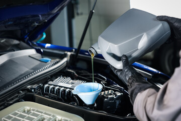 Worker pouring motor oil from canister into car engine, closeup