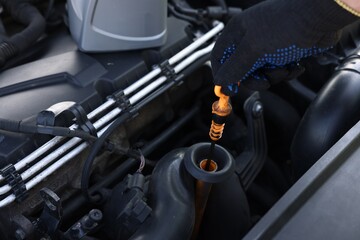 Worker checking motor oil level in car with dipstick, closeup
