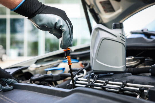 Worker checking motor oil level in car with dipstick, closeup