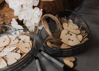 Rustic wedding guest-signing station with wooden heart tokens and twine in glass bowls, black...