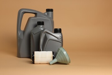 Motor oil in plastic canisters, filter and funnel on beige background, space for text