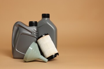 Motor oil in plastic canisters, filter and funnel on beige background, space for text