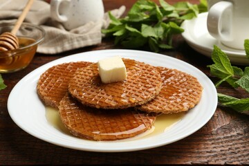 Tasty Dutch waffles (stroopwafels) with honey and butter cube on wooden table, closeup