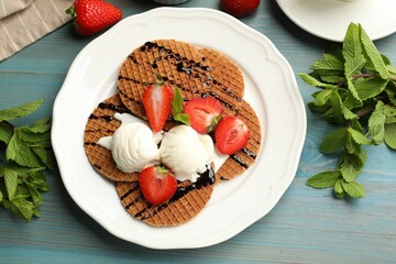Tasty Dutch waffles (stroopwafels) with ice cream, chocolate sauce, mint and strawberries on light blue wooden table, flat lay
